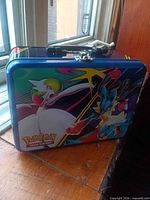 Front view of blue metal Pokémon TCG lunch tin featuring Lucario and Gardevoir
