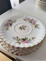 Stack of eight Moss Rose saucers showing floral design and gold rim