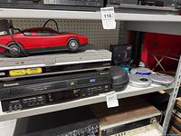 Sony combo player, Panasonic VCR, red car gadget and boxed headphones on shelf