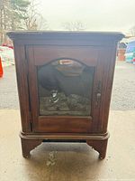 Front view of fireplace heater showing cabinet, glass door and faux logs