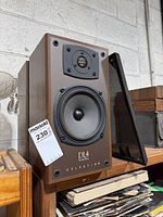 Full view of left speaker with grille removed showing woofer and tweeter plus model marking