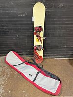 Full view of snowboard standing upright with bindings attached and bag on floor