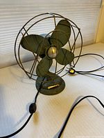 Front angled view showing teal metal four-blade fan, cage, base, and replaced cord with switch