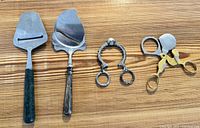 Four kitchen utensils laid out on wood surface: two cheese slicers, ring egg shell cutter, rooster scissor egg topper