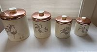 Front view of four graduated canisters with lids on