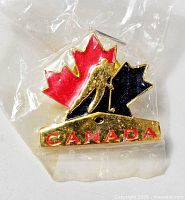 Front view of sealed lapel pin showing red/black maple leaf, hockey player silhouette, CANADA text