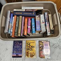 Bin with 25 assorted fiction books showing spines and three featured covers placed in front