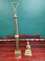 Tall brass lamp column and brass Buddha figurine shown together