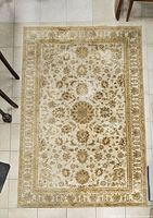 Full view of rectangular beige and gold floral oriental-style rug on tiled floor