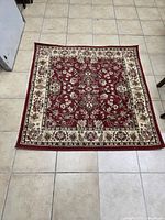 Full view of square red and beige Kashan pattern rug on tile floor