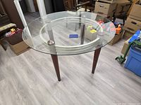 Full view of round glass table showing glass top, metal ring support, and wood legs