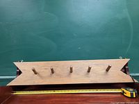 Front view of wooden coat rack showing five pegs and measuring tape for scale
