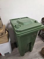 Front left view of the green wheeled garbage can showing lid, body and wheels