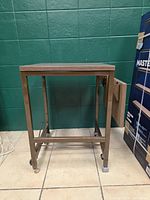 Full view of metal projector table showing frame, casters, and drop shelf folded