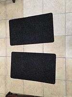 Two small black ribbed floor mats laid side by side on tiled floor