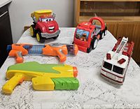 All six toys arranged on table: three vehicles, two Nerf blasters, one water blaster