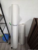 Two partial rolls of transparent vapour barrier standing upright against wall