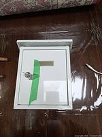 Front view of white metal mailbox showing locking door, key, nameplate window