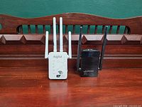 Aigital white WiFi extender with four antennas beside Linoor black extender with two antennas on wooden surface