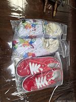 Both pairs of sneakers sealed in plastic bags: multicolour pair on top, red pair below