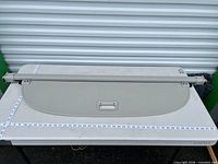 Full view of beige retractable cargo cover laid flat with measuring tape for scale