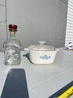 Casserole with lid beside glass bottle showing overall appearance