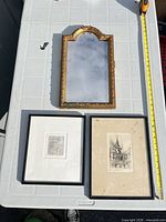 Group shot of gilt mirror and two framed etchings on table with tape for scale