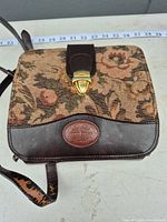 Front view showing floral tapestry panel, leather trim, logo patch, clasp and measuring tape