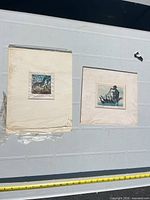 Two mounted small square relief prints on large white boards side by side on measurement board