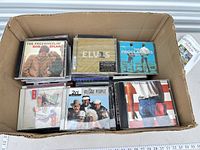 Box containing numerous CDs; visible titles include Bob Dylan, Elvis Presley, The Proclaimers, Village People and others