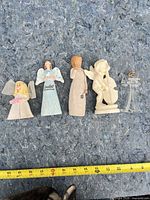 Group of five angel figurines aligned on blanket with tape measure showing size reference