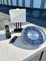 Group shot of all four items: wall clock, table lamp, cordless phone on base, remote