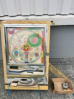 Full front view of Nishijin pachinko machine on blue wire stand with cardboard box of balls