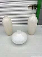 Front view of two tall bottle-form vases and one squat round vase