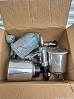 Open box showing spray guns, air ratchet, impact tool, paint cups and fittings