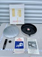 all components laid out: pan, lid (wrapped), handle, knob, leaflets, box