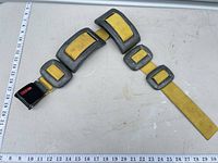 Full view of yellow aircraft lap belt with cast aluminum slides and latch showing length against ruler