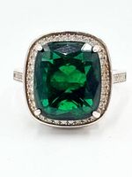 Front view of ring showing cushion-cut green gemstone, halo of clear stones, four prongs