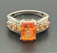 Top view of ring showing center emerald-cut orange stone and side accent stones