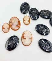 Group view of peach/ivory female cameos and dark grey dragon cameos on white surface