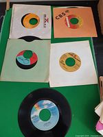 Five records in paper sleeves displayed on green surface