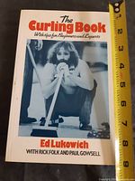 Front cover of paperback curling instruction book with tape measure indicating size