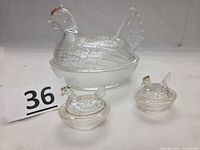 three clear glass hen-on-nest dishes, one large two small