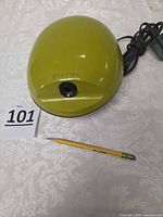 Top view of Boston avocado green electric pencil sharpener with power cord and sample pencil