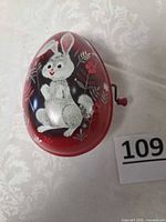 Side view of red tin Easter egg with rabbit graphic and crank
