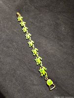 Full view of bracelet with green enamel frog links on black background
