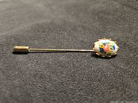 Full view of stick pin showing porcelain floral cabochon and gold-tone pin