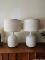 Both matching off-white textured table lamps on wooden surface