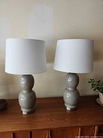 Front view of both grey glass table lamps with shades on wooden surface