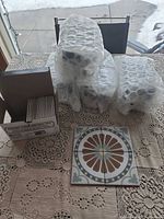 Four bubble-wrapped sealed boxes, one open partial box showing stacked square tiles, and four tiles laid out to display pattern